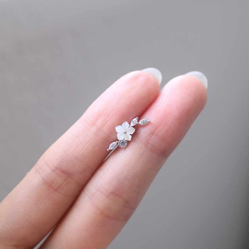 Pode incluir: Um brinco delicado de prata com um design de flor e folha com pedras brancas.