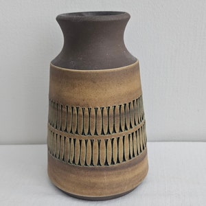 Puede incluir: Un jarrón de cerámica marrón y beige con un patrón geométrico. El jarrón tiene una base ancha y un cuello estrecho.