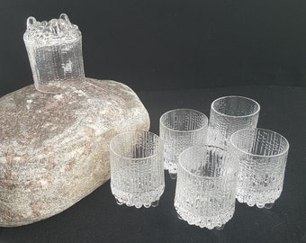 May include: Set of six clear glass shot glasses with a textured design. The glasses are arranged in a semi-circle on a gray surface.