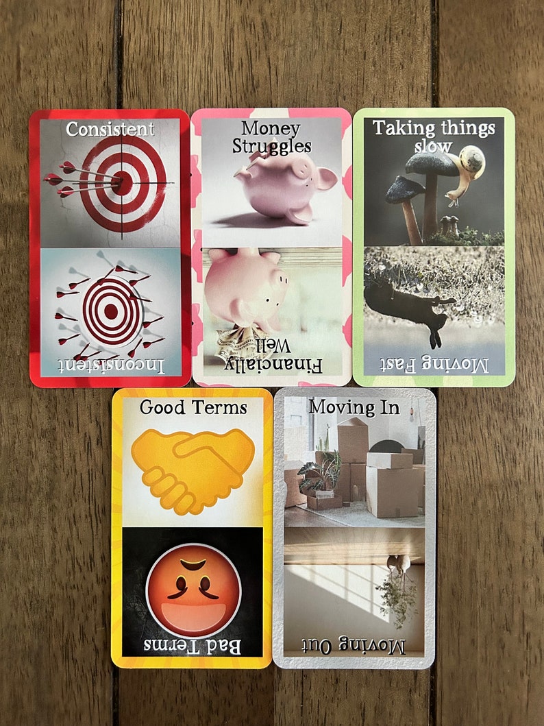 May include: Five colorful cards with different images and text. The cards are laid out in a row on a wooden surface. The text on the cards includes "Consistent", "Money Struggles", "Taking things slow", "Good Terms", "Bad Terms", "Moving In", and "Moving Out".