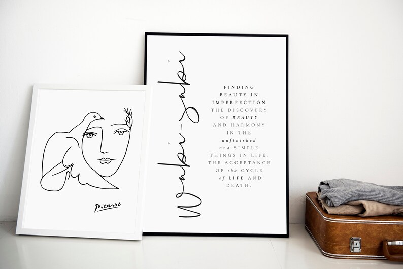 May include: Two black and white framed prints on a white wall. The print on the left is a line drawing of a woman's face with a dove. The print on the right has the text "Waki-jabi" and a quote about finding beauty in imperfection.