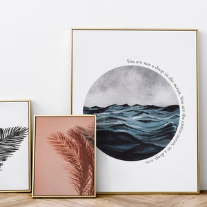 May include: Three framed prints with gold frames. The leftmost print features a black and white illustration of a palm leaf. The center print features a pink background with a brown palm leaf shadow. The rightmost print features a blue watercolor painting of ocean waves with the text "You are not a drop in the ocean. You are the entire ocean, in a drop."