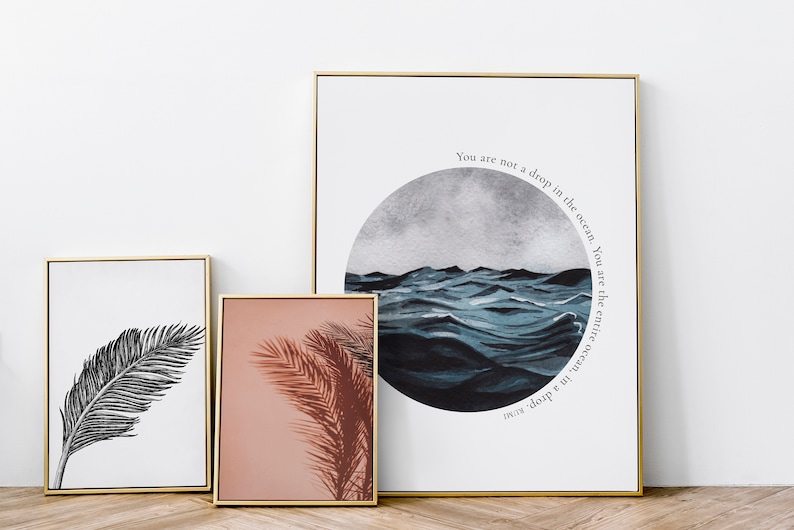 May include: Three framed prints with gold frames. The leftmost print features a black and white illustration of a palm leaf. The center print features a pink background with a brown palm leaf shadow. The rightmost print features a blue watercolor painting of ocean waves with the text "You are not a drop in the ocean. You are the entire ocean, in a drop."