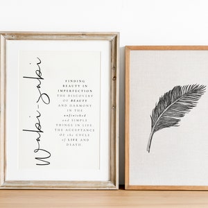 May include: Two framed prints, one with a black and white illustration of a feather and the other with a quote about finding beauty in imperfection. The quote reads "Finding beauty in imperfection, the discovery of beauty and harmony in the unfinished and simple things in life. The acceptance of the cycle of life and death."