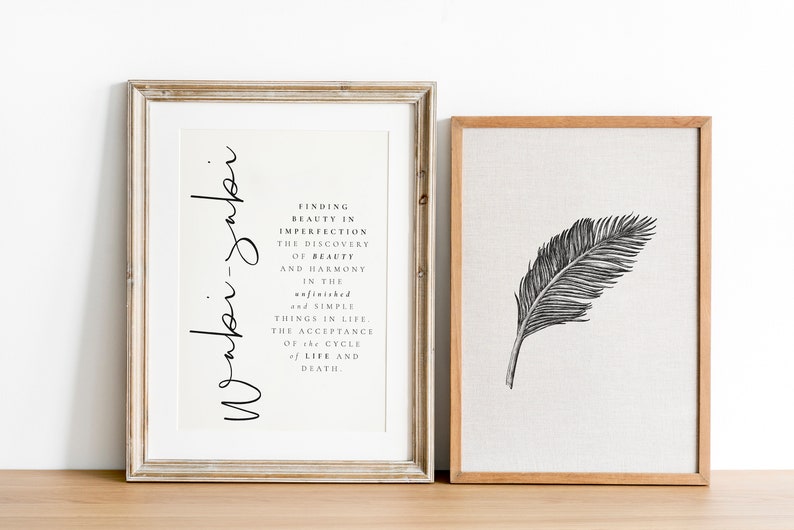May include: Two framed prints, one with a black and white illustration of a feather and the other with a quote about finding beauty in imperfection. The quote reads "Finding beauty in imperfection, the discovery of beauty and harmony in the unfinished and simple things in life. The acceptance of the cycle of life and death."