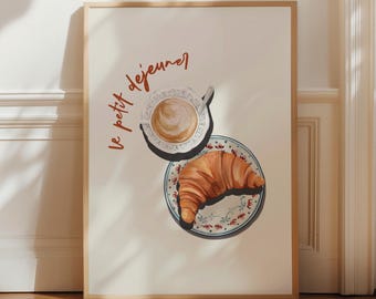 May include: A framed wall art print featuring a top-down illustration of a golden-brown croissant on a floral patterned plate next to a cup of coffee with latte art. The text le petit dejeuner is written in a cursive orange script on the left side.
