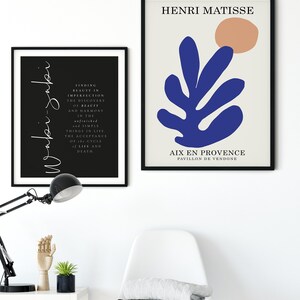 May include: Two framed prints, one with a black background and white text, the other with a white background and a blue abstract leaf design with a peach circle. The text on the black print reads "Finding beauty in imperfection, the discovery of beauty and harmony in the unfinished and simple things in life. The acceptance of the cycle of life and death." The text on the white print reads "Henri Matisse" and "Aix en Provence, Pavillon de Vendome".