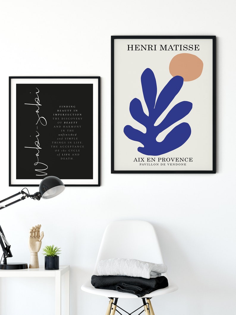 May include: Two framed prints, one with a black background and white text, the other with a white background and a blue abstract leaf design with a peach circle. The text on the black print reads "Finding beauty in imperfection, the discovery of beauty and harmony in the unfinished and simple things in life. The acceptance of the cycle of life and death." The text on the white print reads "Henri Matisse" and "Aix en Provence, Pavillon de Vendome".