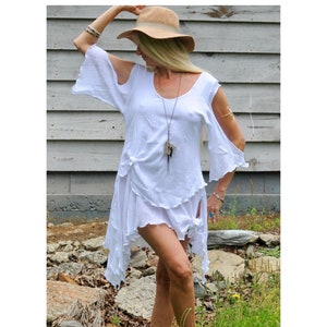 May include: White, flowy, off-the-shoulder dress with a ruffled hem and a knotted detail at the waist. The dress is worn by a person with long blonde hair and a straw hat.