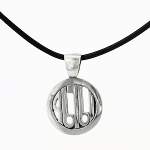 May include: A silver pendant necklace with a circular design. The pendant features a stylized design within a circular frame, suspended from a black cord. The pendant is made of a shiny, metallic material.