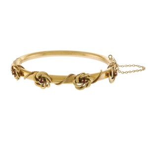 Puede incluir: Un brazalete de oro con un diseño de cuerda trenzada y tres acentos de piedras preciosas rojas.