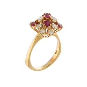 Puede incluir: Un anillo de oro con un grupo de piedras preciosas. El centro del anillo presenta un diseño floral de rubíes rojos y diamantes blancos brillantes. La banda es de oro pulido.