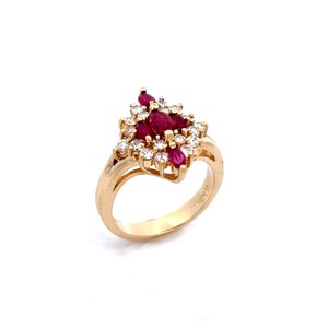 May include: A gold ring featuring a cluster of marquise-cut red rubies at the center, surrounded by a halo of small, round, clear white diamonds. The band is crafted from polished yellow gold, showcasing a classic, multi-stone setting design.