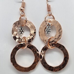 May include: Rose gold hammered metal earrings with two circles and a small silver charm.