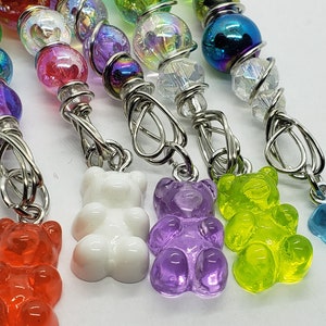 May include: A set of six gummy bear charms, each a different color, hanging from silver wire wrapped with iridescent beads. The charms are attached to silver jump rings.