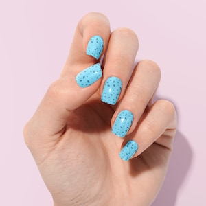 Può includere: Una mano con smalto per unghie blu chiaro con un design bianco maculato.