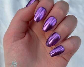 Op de afbeelding: Paarse metallic press-on nagels met een kistvorm. De nagels zitten op een hand met een witte achtergrond. De afbeelding bevat de tekst "Nail Bella Custom Press On Nails".