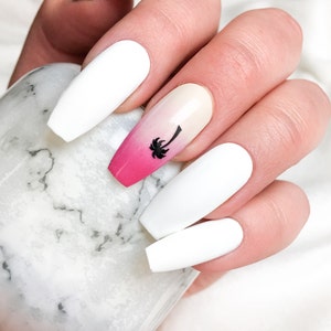 Pode incluir: Unhas postiças brancas longas em forma de caixão com um design degradê rosa e branco em uma unha com uma silhueta de palmeira preta.