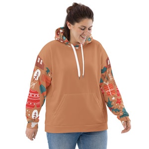 May include: A brown oversized hoodie with a white drawstring. The sleeves feature a colorful Christmas pattern with illustrations of presents, ornaments, and snowflakes.