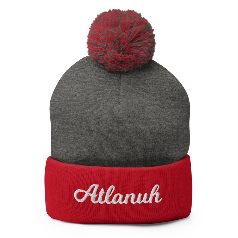 May include: Gray and red knit beanie with a pom pom on top. The beanie has a red cuff with the word "Atlanuh" embroidered in white.