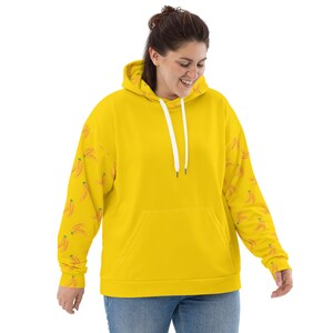 May include: A yellow hoodie with a white drawstring and a kangaroo pocket. The sleeves have a pattern of small orange bananas.
