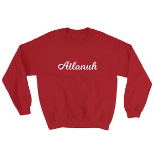May include: Red sweatshirt with white cursive text that reads "Atlanuh"