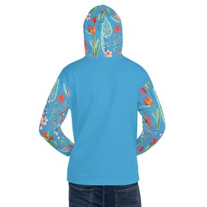 May include: A light blue hoodie with a floral print on the sleeves. The print features a variety of flowers and leaves in shades of red, orange, yellow, green, and white.