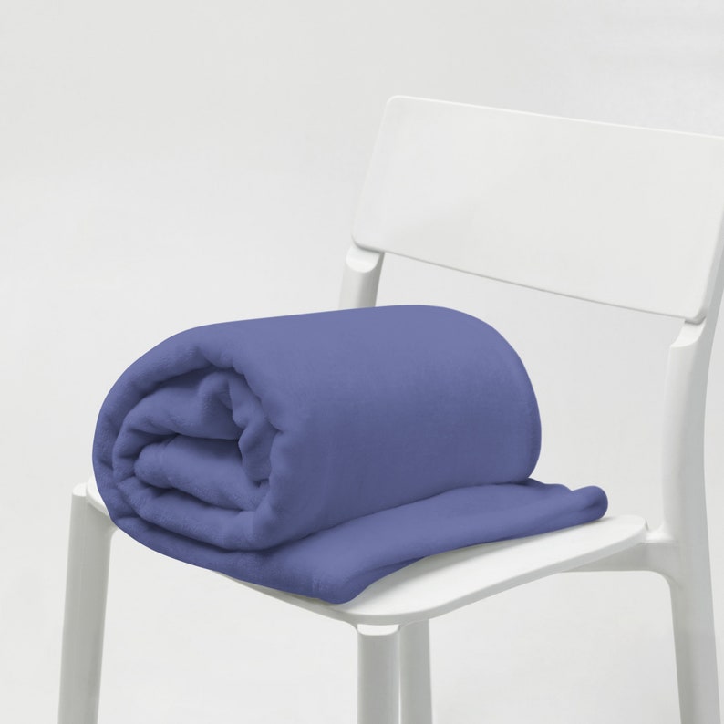 May include: A soft, blue fleece blanket folded and placed on a white chair. The blanket is a solid color with no patterns.