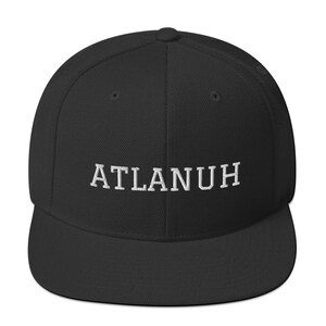 May include: A black baseball cap with a flat brim. The embroidered text "ATLANUH" is displayed in white across the front of the cap. The cap has a structured fit and a rounded crown.