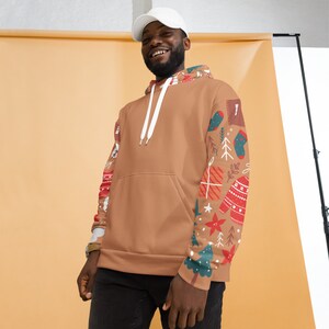 May include: A brown hoodie with a white drawstring and a Christmas-themed design on the sleeves. The design features trees, stars, presents, and a sweater.