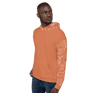 May include: A rust-colored hoodie with a white leaf pattern on the sleeve. The hoodie has a drawstring hood and a kangaroo pocket.
