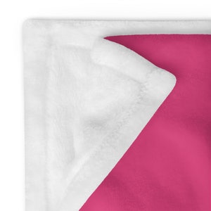 May include: A soft, plush blanket with a white side and a bright pink side. The blanket is folded in half, showing both sides.
