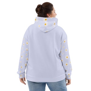 May include: A light blue hooded sweatshirt with a daisy print on the sleeves and hood. The hoodie has a relaxed fit and a drawstring hood.