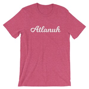 May include: A pink heather t-shirt with a white cursive font that reads "Atlanuh".