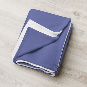 May include: A soft, plush blanket with a blue side and a white side. The blanket is folded in half and is lying on a wooden surface.