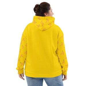 May include: A yellow hoodie with a banana pattern on the sleeves. The hoodie has a drawstring hood and a kangaroo pocket.