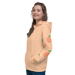 May include: A peach-colored hoodie with a pattern of peaches on the sleeves. The hoodie has a drawstring hood and a kangaroo pocket.