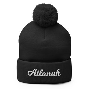 May include: Black knit beanie with a fluffy pom pom on top and the word "Atlanuh" embroidered in white on the cuff.