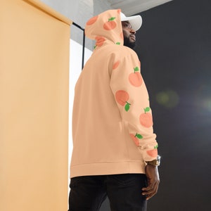 May include: A peach-colored hoodie with a peach print on the sleeve. The hoodie has a drawstring hood and a kangaroo pocket.