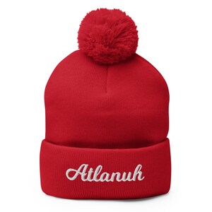 May include: Red knit beanie with a white pom pom on top and the word "Atlanuh" embroidered in white on the cuff.