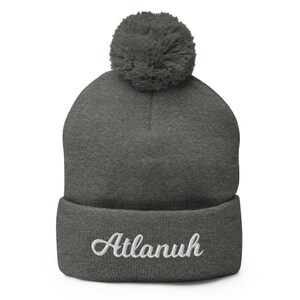 May include: Gray knit beanie with a pom pom on top and the word "Atlanuh" embroidered in white on the cuff.