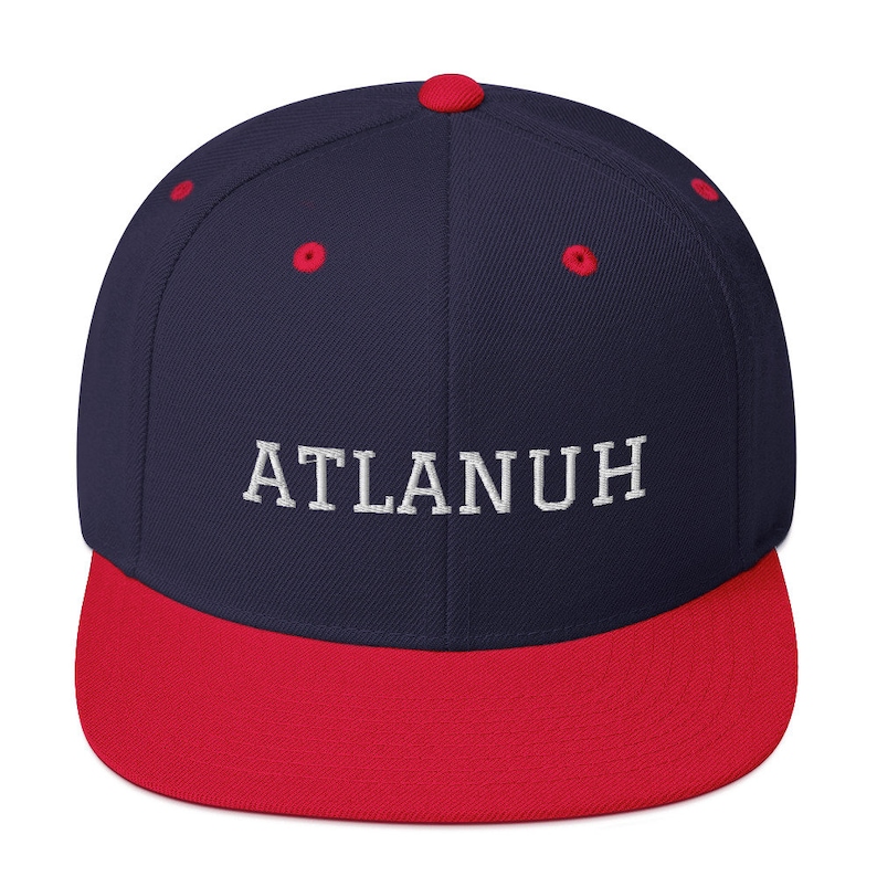 May include: A navy blue baseball cap with a red brim and top button. The embroidered text "ATLANUH" is in white. This hat is a stylish accessory for casual wear.