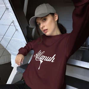 May include: A maroon sweatshirt with a white graphic of the word "Alanuh" in a stylized font. The sweatshirt has long sleeves and a crew neck.