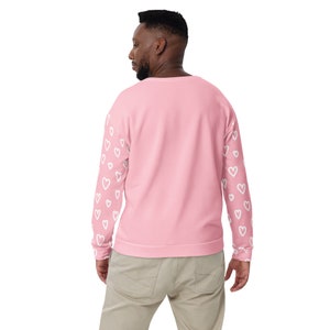 May include: A pink sweatshirt with white heart designs on the sleeves. The sweatshirt has a crew neck and long sleeves.