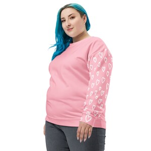 May include: A pink sweatshirt with white heart designs on one sleeve. The sweatshirt is worn by a person with blue hair.