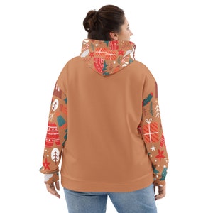 May include: A brown hoodie with a Christmas-themed pattern on the sleeves and hood. The pattern includes presents, candy canes, snowflakes, and trees. The hoodie has a drawstring hood and a kangaroo pocket.