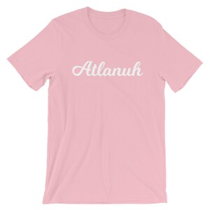 May include: A pink t-shirt with the word "Atlanuh" printed in white cursive lettering.