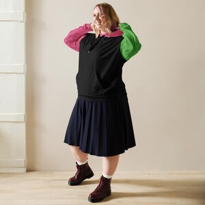 May include: A black hoodie with pink and green sleeves, paired with a navy blue pleated skirt and burgundy boots. The person is wearing white socks. The outfit is casual and stylish.