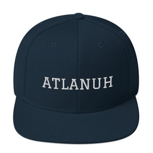 May include: A navy blue baseball cap with a flat brim. The embroidered text "ATLANUH" is in white, centered on the front of the cap. The cap has a structured fit and a rounded crown.