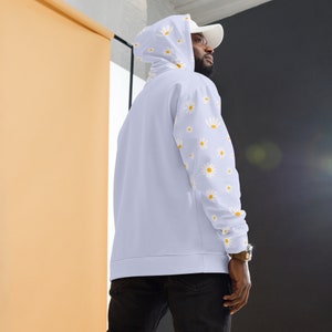 May include: A light blue hoodie with a white daisy pattern on the sleeves. The hoodie has a drawstring hood and a kangaroo pocket.